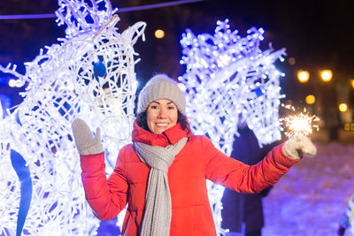 Portrait of smiling woman standing against illuminated christmas tree at night