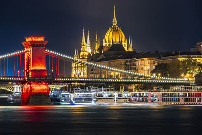 Illuminated bridge over river against hungarian parliament building at night