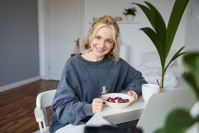 Portrait of young woman holding christmas tree at home