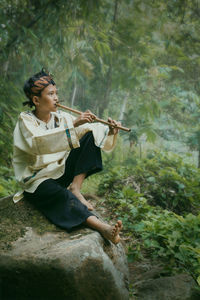 Full length of boy playing flute sitting on rock