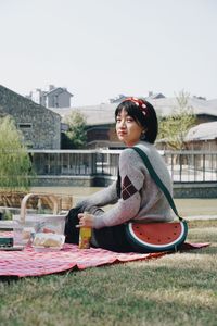 Side view of boy sitting on grass against sky