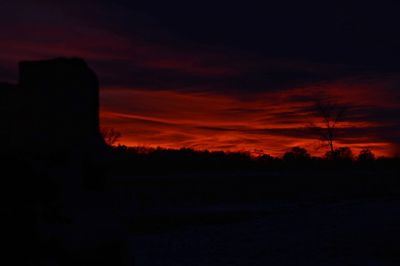 Silhouette trees on field against dramatic sky during sunset