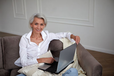 Portrait of businesswoman using laptop sitting on sofa at home