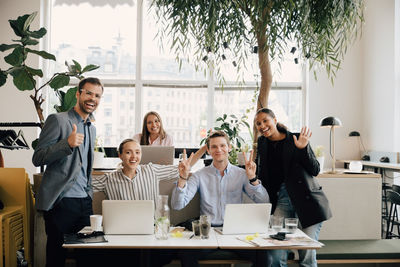 Portrait of smiling colleagues with laptops gesturing at desk in coworking space