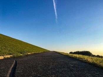 Road amidst field against clear blue sky