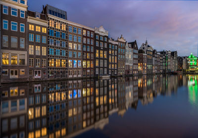 Illuminated buildings reflecting on calm lake against sky at dusk