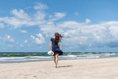 Rear view of woman standing at beach against sky