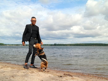 Portrait of man with dog standing on beach against sky