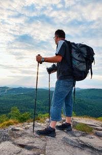 Professional photographer with big mirror camera on neck on peak. hilly land, spring green valley