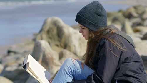 Midsection of woman wearing hat sitting by sea