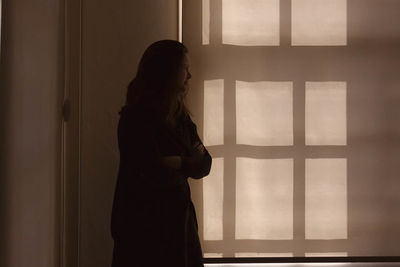 Pensive woman standing by window at home