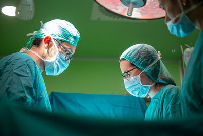 Side view of doctor and assistants in medical uniform performing surgery through cut on patient in modern hospital