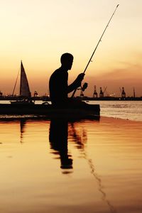 Silhouette man fishing in sea against sky during sunset