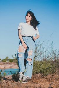 Portrait of young woman standing on field against clear sky