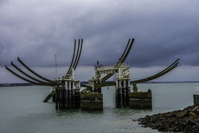 Cranes by sea against sky