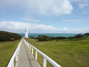 Footpath leading to calm sea against cloudy sky