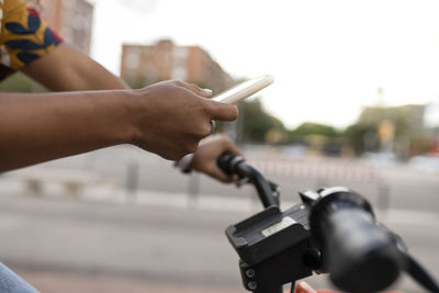 Hand of woman using smart phone and riding bicycle at footpath