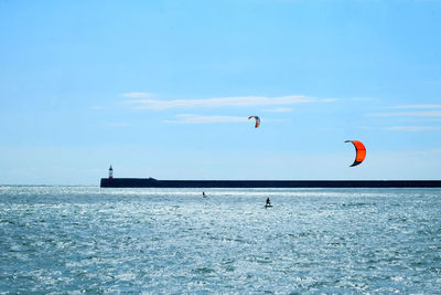 Distant view of people kiteboarding in sea against blue sky