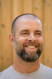 Portrait of the handsome man with beard smiling standing against wooden background