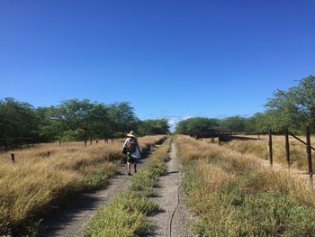 Rear view of woman walking on road amidst field against clear sky