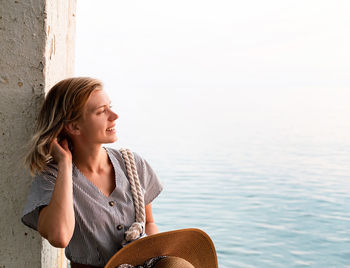 Young woman looking away while sitting by sea