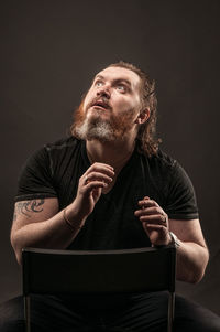 Young man looking away while sitting against black background