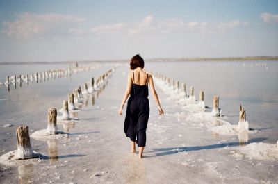 Rear view of woman walking on beach against sky