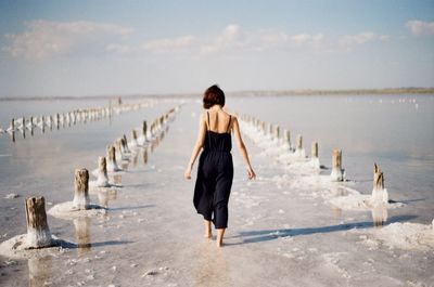 Rear view of woman walking on beach against sky