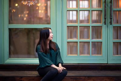 Woman looking away while sitting hardwood floor by window