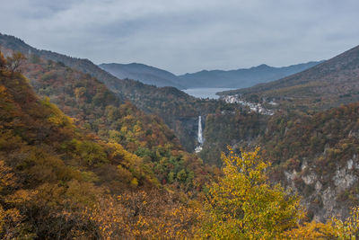 Scenic view of waterfall amidst tree and mountain against cloudy sky
