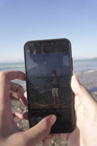 Midsection of person photographing sea against sky