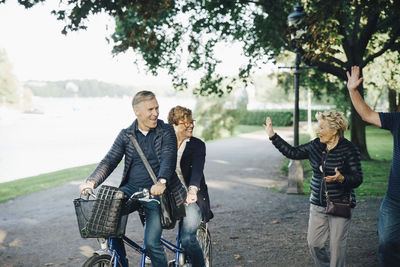 Senior couple waving friends riding tandem bike in park