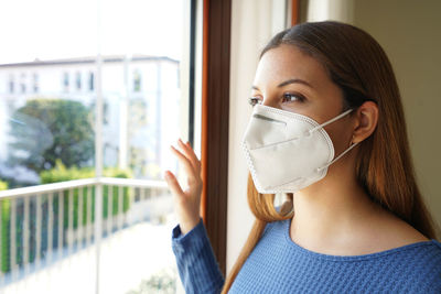 Young woman wearing mask looking out of window