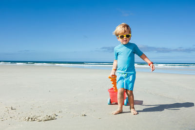 Full length of boy standing at beach against sky