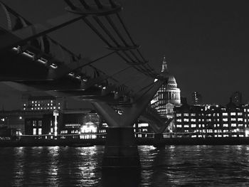 Illuminated bridge over river by buildings against sky at night