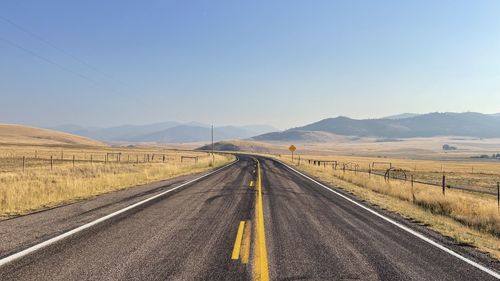 Road amidst field against clear sky