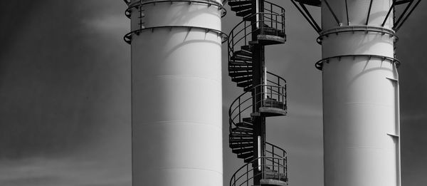 Section of a metal spiral staircase on an industrial building with two chimneys in black and white
