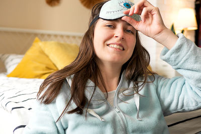 Middle aged woman in pajamas and sleep mask sitting relaxed on bed at home