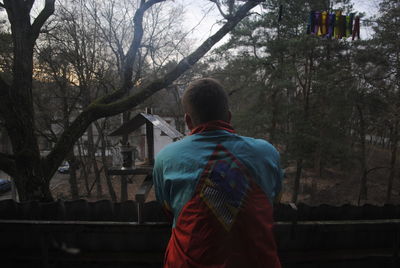 Rear view of man standing in balcony against trees