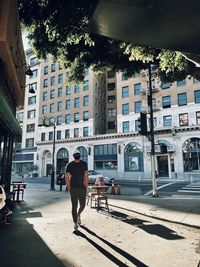 Rear view of man walking on street against buildings in city