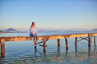 Woman sitting on pier in sea against clear sky