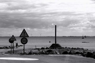 Road signs by sea against cloudy sky