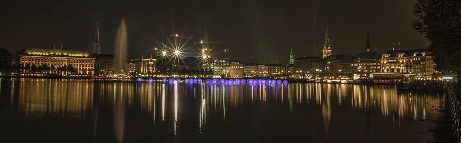 Illuminated city by river against sky at night