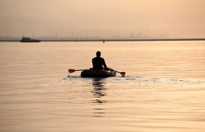 Rear view of man sailing boat on sea against sky