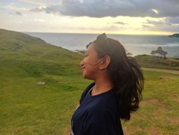 Side view of young woman standing on field against sky during sunset