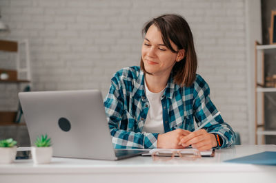 Young woman using mobile phone while sitting on table