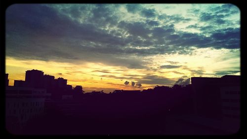 Silhouette of buildings against cloudy sky at sunset