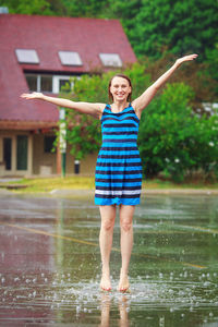 Portrait of smiling woman standing with arms outstretched during rainy season