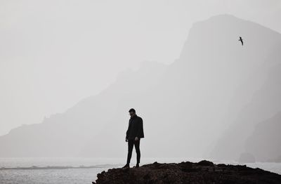 Young man looking away standing on rock by sea