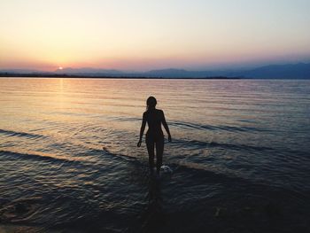 Silhouette man standing in sea against sky during sunset